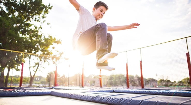 A boy jumping around on an outdoor trampoline