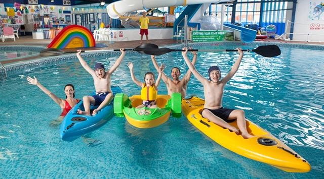 A family posing for a photo in kayaks in the indoor swimming pool