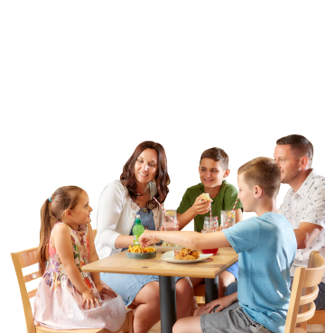 Family of five sat around a wooden table eating, drinking and smiling