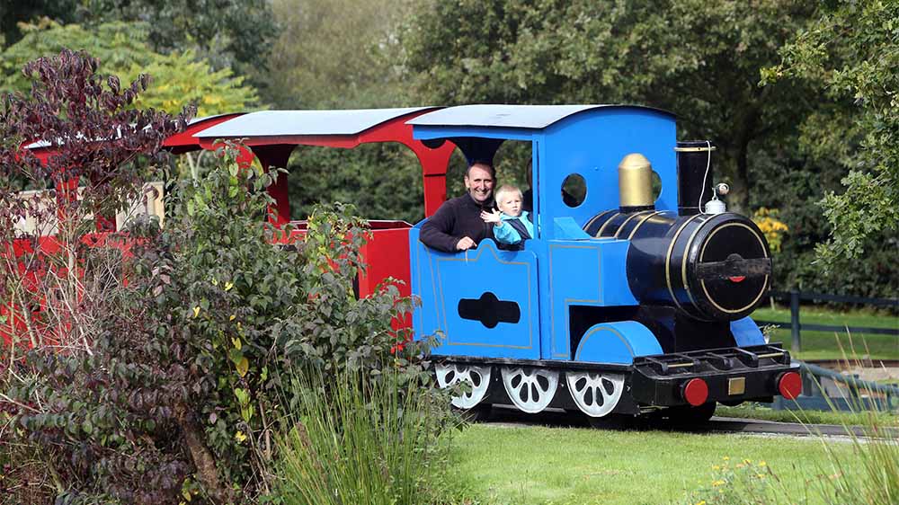 A dad and his kid riding on a miniature train ride through a park