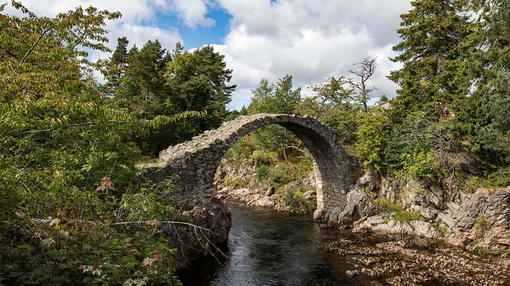 An ancient eroded stone bridge crossing a river in the Scottish Highlands
