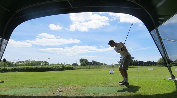 man swinging a golf club on a driving range on a sunny day