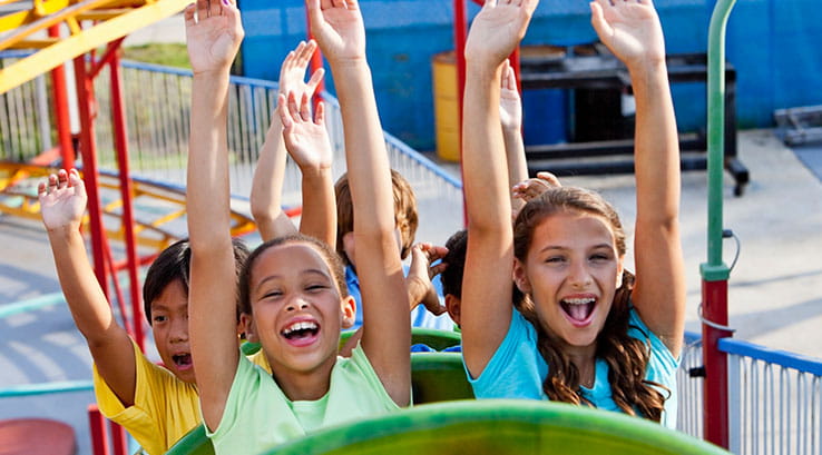 Kids riding a rollercoaster with their arms in the air