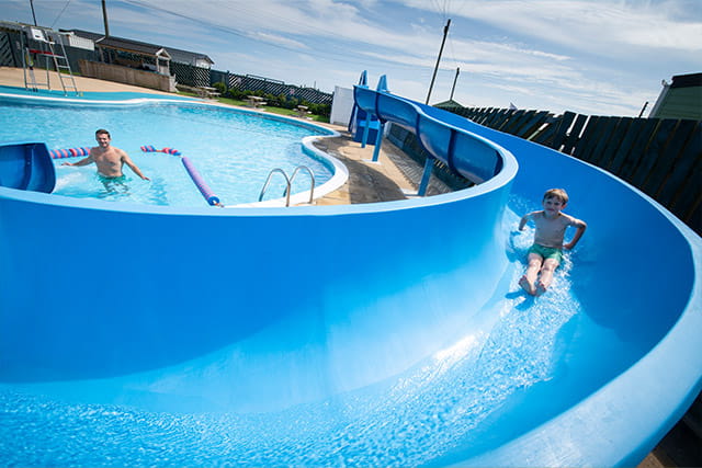 A boy sliding down the waterslide into the outdoor swimming pool at Barmston Beach Holiday Park