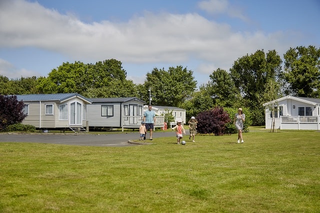 A family playing football in front of their holiday accommodation at Breydon Water Holiday Park