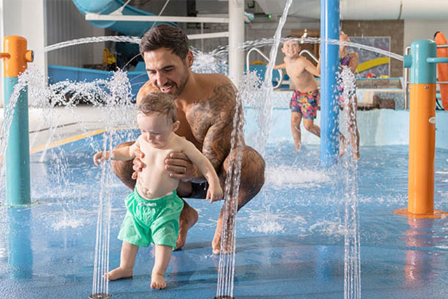 A dad and toddler playing in the fountains of the indoor pool at Carmarthen Bay