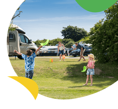 A family playing ball games in the camping field at Hollywell Bay