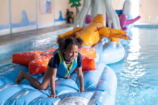 young girl having fun on inflatables in the indoor swimming pool