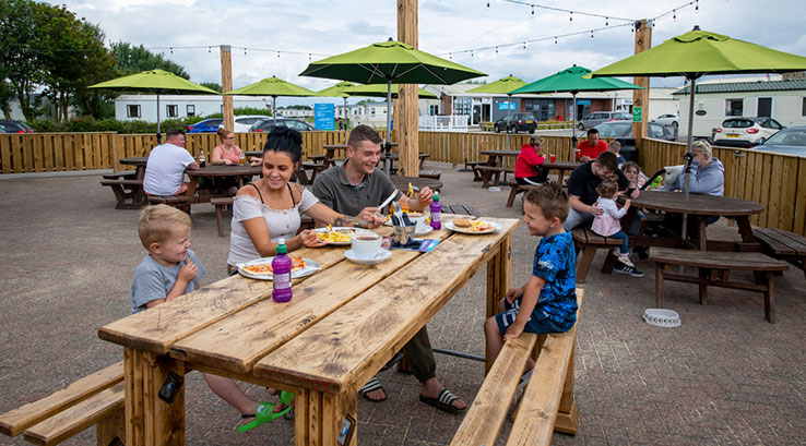 A family enjoying an outdoor meal on a picnic bench at Skipsea Sands Holiday Park