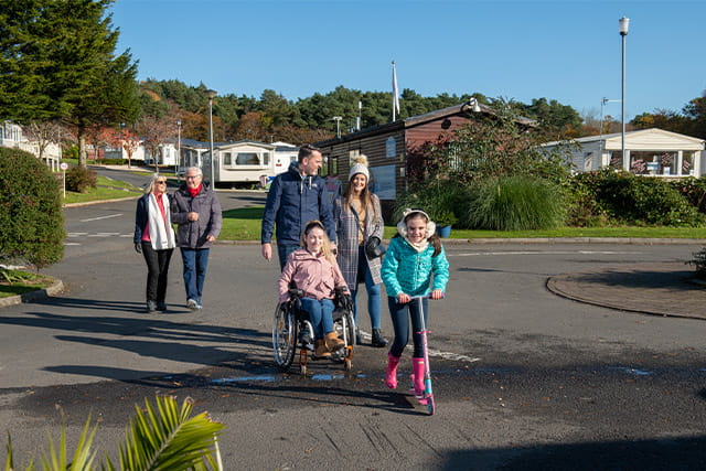 A family with a girl in a wheelchair going for a walk past caravans at Sundrum Castle Holiday Park