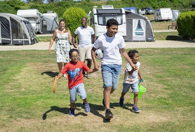 A family walking through the sunny touring and camping field at West Bay Holiday Park