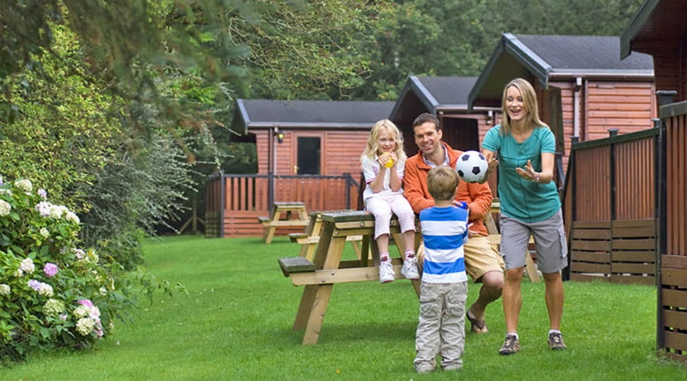 A family playing with a football on the grass outside their lodge