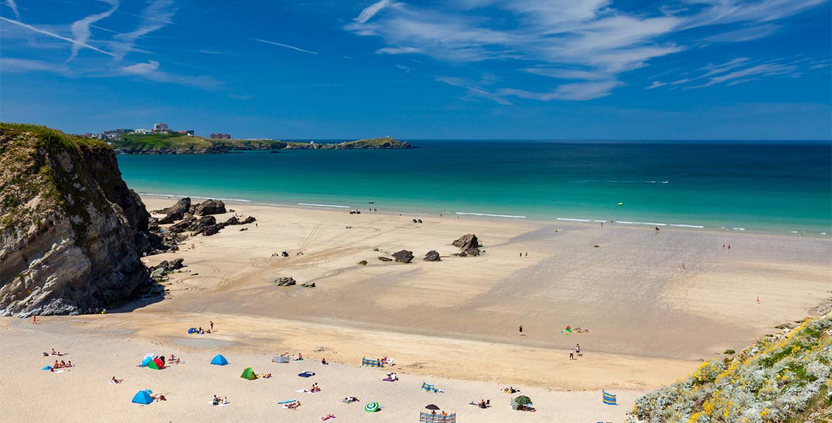 A sandy beach with clear blue waters looking across the bay to Newquay in Cornwall