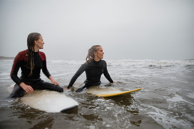 Two friends sitting on surfboards in the rain