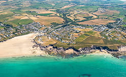 An aerial view over Polzeath surrounded by lush green fields, white sandy beaches and vibrant blue sea