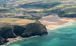 An aerial view of the dramatic coastline and white sandy beach of St Mawgan in Cornwall