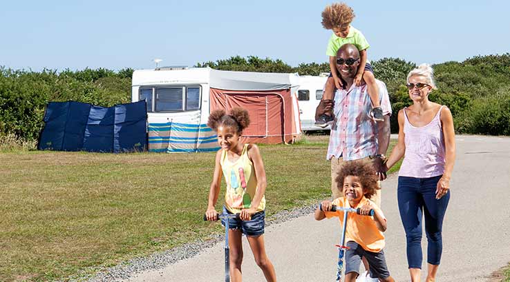 Family walking and children on scooters on camp site site path on sunny day