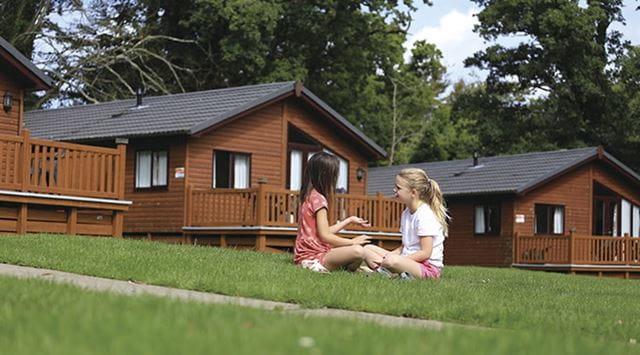 Two girls sitting on the grass outside wooden lodges