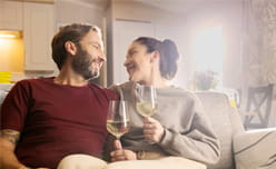 Couple holding a glass of white wine sat on the sofa