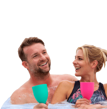 Man and woman sat smiling in a hot tub holding green and pink plastic wine glasses