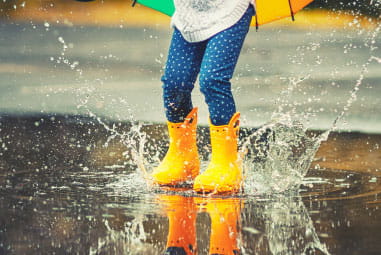 a child jumping in a puddle with yellow wellies on