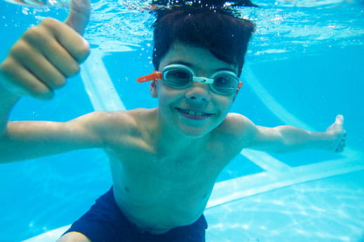 Little boy wearing swimming goggles smiling underwater