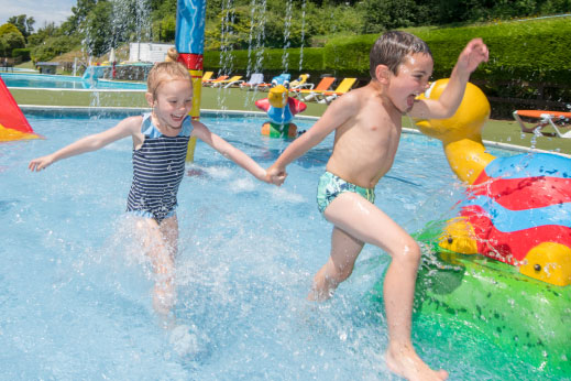 Children holding hands jumping into an outdoor pool
